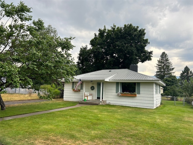 view of front of house featuring a chimney, fence, metal roof, and a front yard