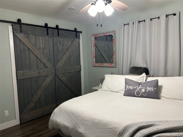 bedroom with ceiling fan, a barn door, and dark wood-style flooring