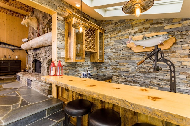 interior space featuring hanging light fixtures, stone finish flooring, a sink, a stone fireplace, and wet bar