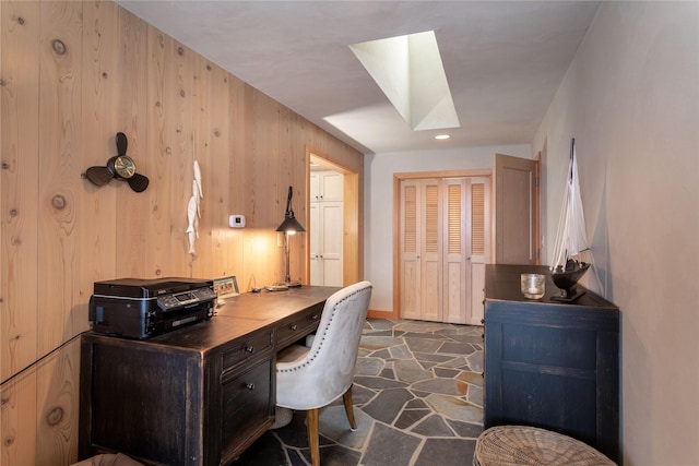 office featuring baseboards, wood walls, a skylight, and stone tile floors