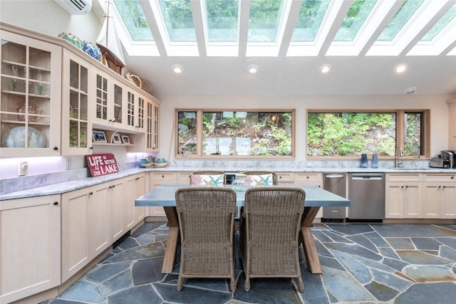 kitchen with vaulted ceiling with skylight, recessed lighting, stone tile floors, dishwasher, and glass insert cabinets