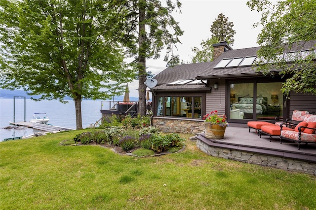 back of house featuring stone siding, a chimney, roof with shingles, a water view, and a yard