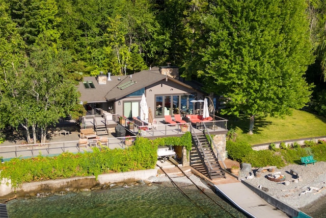 back of house with roof with shingles, a patio, a chimney, a wooden deck, and stairs