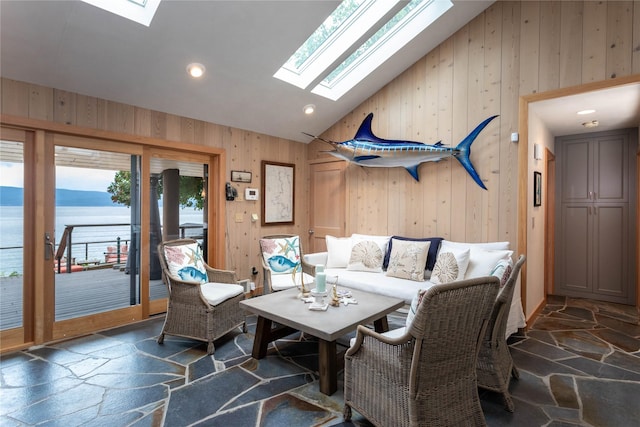 living area with high vaulted ceiling, a skylight, wooden walls, and stone tile floors