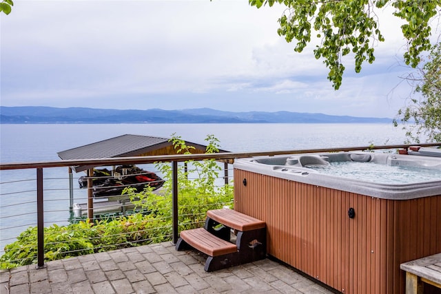 view of patio / terrace with a balcony, a water and mountain view, and a hot tub