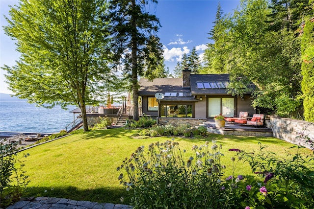 back of house with a patio, a deck with water view, stairs, a lawn, and a chimney