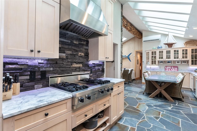 kitchen with lofted ceiling with beams, a wall unit AC, wall chimney exhaust hood, stone tile flooring, and stainless steel gas stovetop