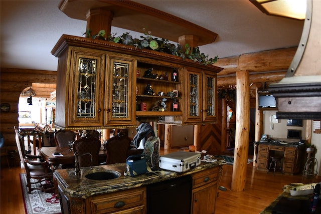 kitchen with wood finished floors, a sink, brown cabinets, dark stone countertops, and glass insert cabinets