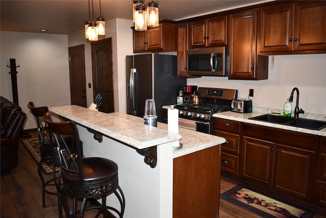 kitchen with a breakfast bar area, a sink, appliances with stainless steel finishes, a center island, and decorative light fixtures