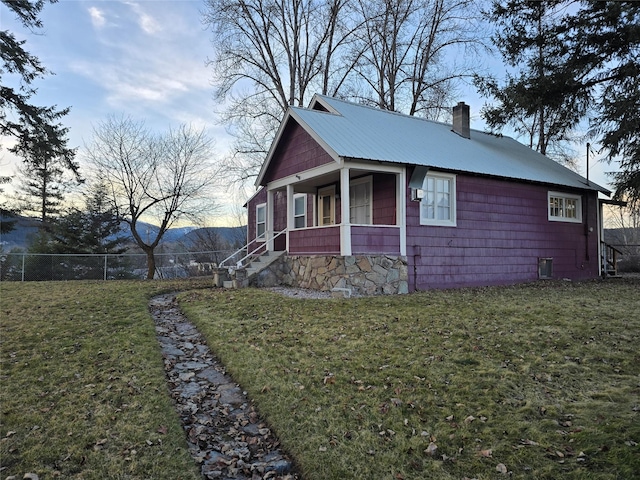 view of side of property with a chimney, a porch, a lawn, metal roof, and fence