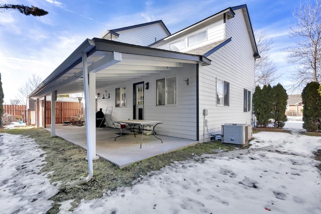 snow covered rear of property with fence and a patio