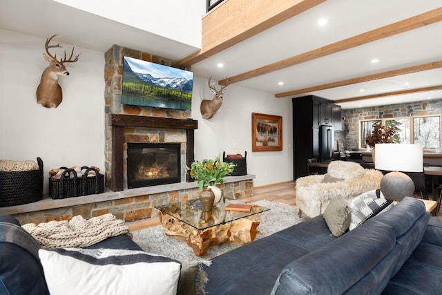 living room with light wood-type flooring, beam ceiling, a stone fireplace, and recessed lighting