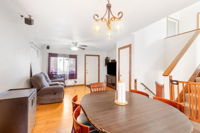 dining area featuring light wood-style floors, stairs, baseboards, and ceiling fan with notable chandelier