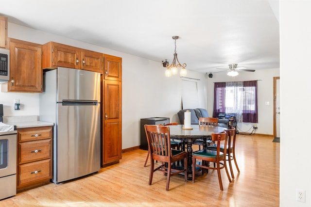 dining space featuring light wood-type flooring, baseboards, and ceiling fan with notable chandelier