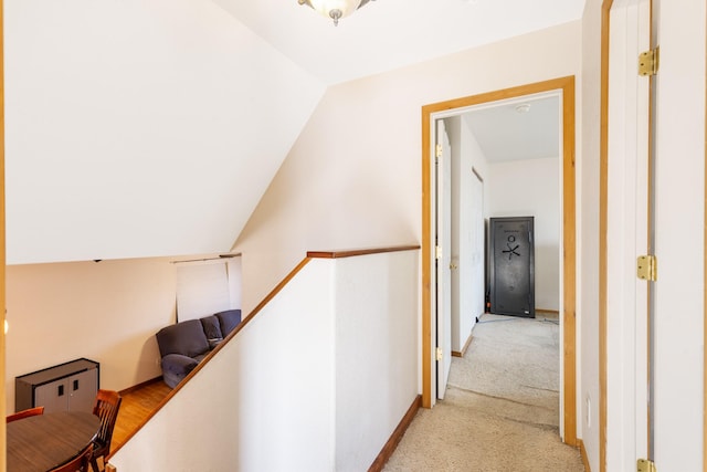 hallway featuring lofted ceiling, baseboards, light colored carpet, and an upstairs landing