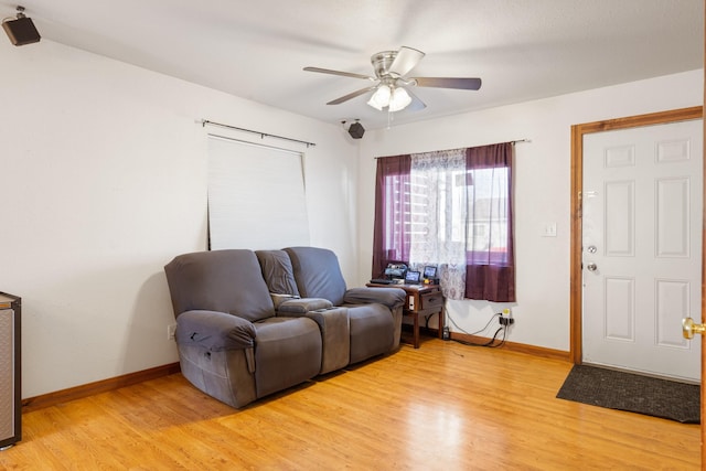 living area featuring light wood-type flooring, baseboards, and a ceiling fan