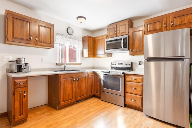 kitchen featuring light countertops, appliances with stainless steel finishes, a sink, and brown cabinets