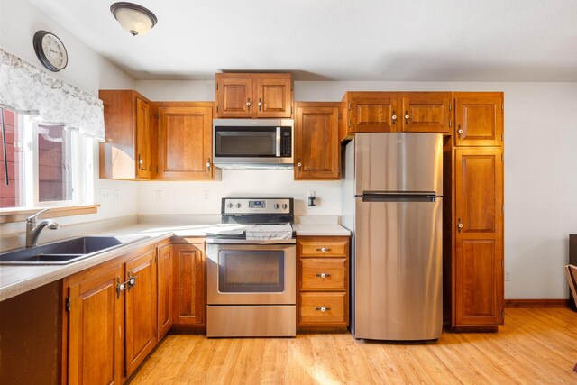 kitchen featuring appliances with stainless steel finishes, brown cabinets, light countertops, light wood-style floors, and a sink