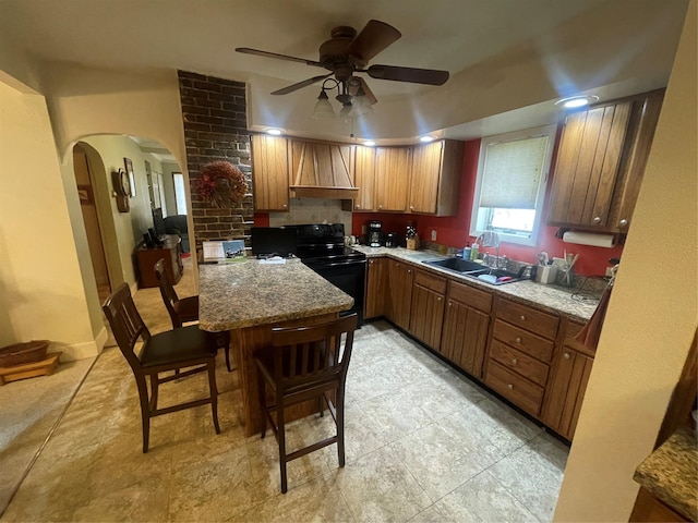 kitchen featuring arched walkways, brown cabinets, custom range hood, a sink, and black / electric stove