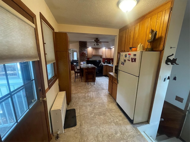 kitchen with brown cabinets, radiator heating unit, a ceiling fan, freestanding refrigerator, and a textured ceiling