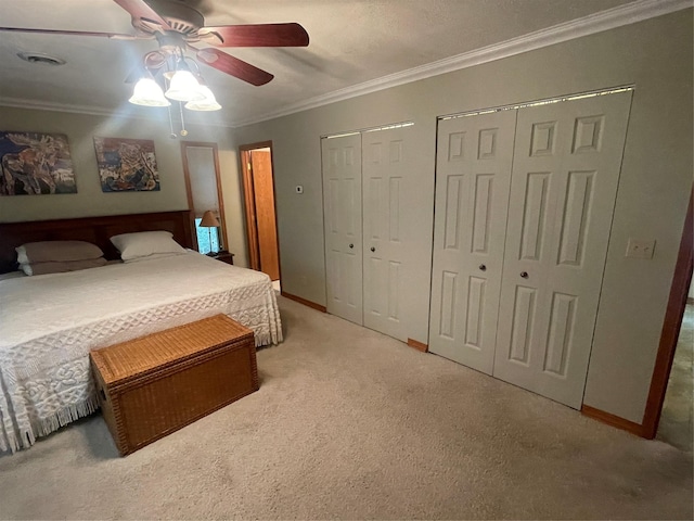 carpeted bedroom featuring visible vents, baseboards, a ceiling fan, crown molding, and two closets