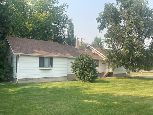 back of house with entry steps, roof with shingles, a yard, and a chimney