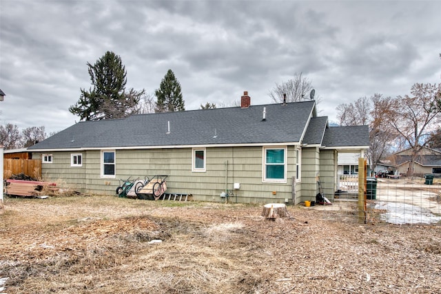 back of house featuring a shingled roof, a chimney, and fence