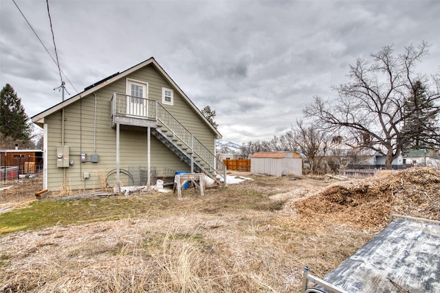 back of house featuring an outbuilding, fence, stairway, and a shed