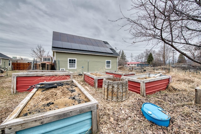 back of house with a garden, metal roof, a standing seam roof, fence, and roof mounted solar panels