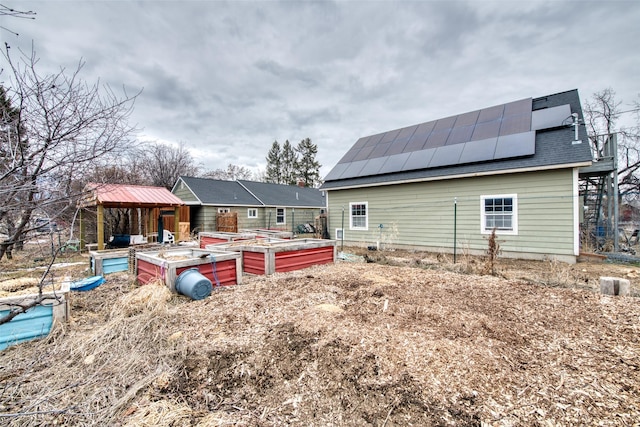 back of property with a standing seam roof, a vegetable garden, metal roof, and solar panels