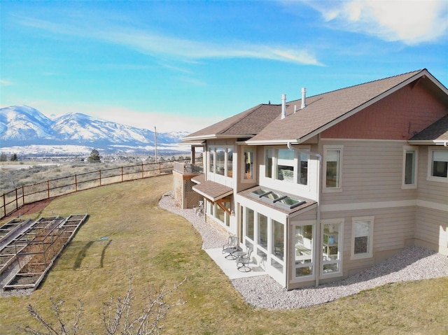 back of house with roof with shingles, a yard, a sunroom, a mountain view, and a fenced backyard