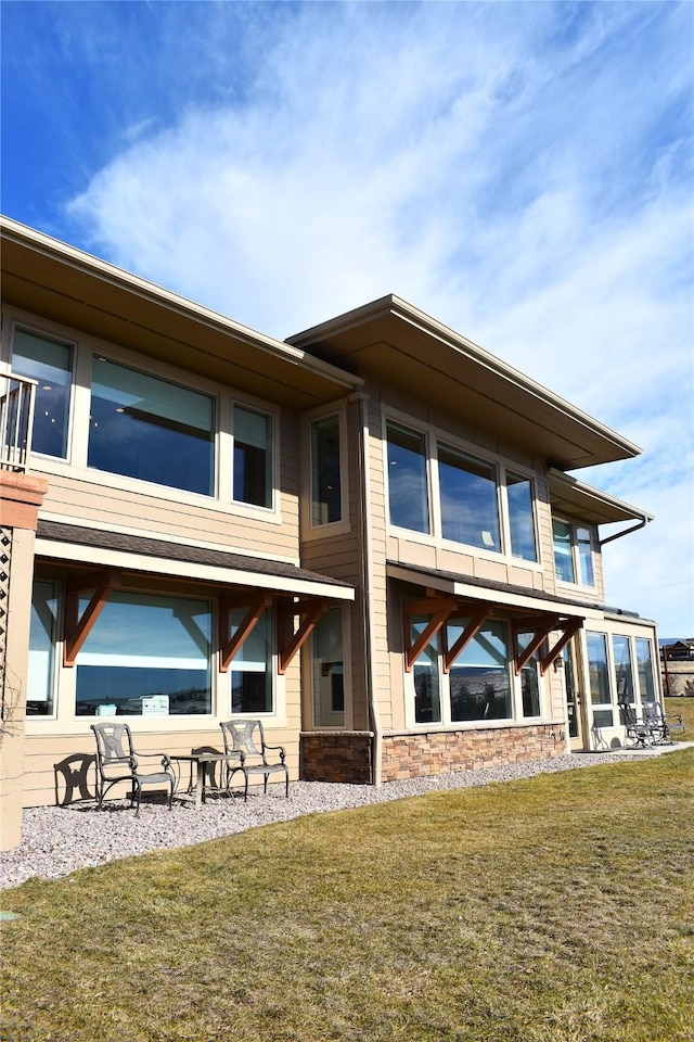 rear view of property with stone siding, a lawn, and a sunroom