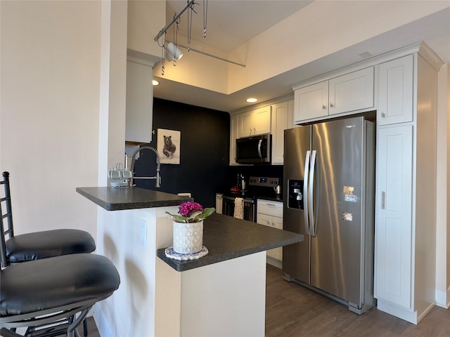 kitchen with stainless steel appliances, a breakfast bar, a peninsula, dark countertops, and dark wood finished floors