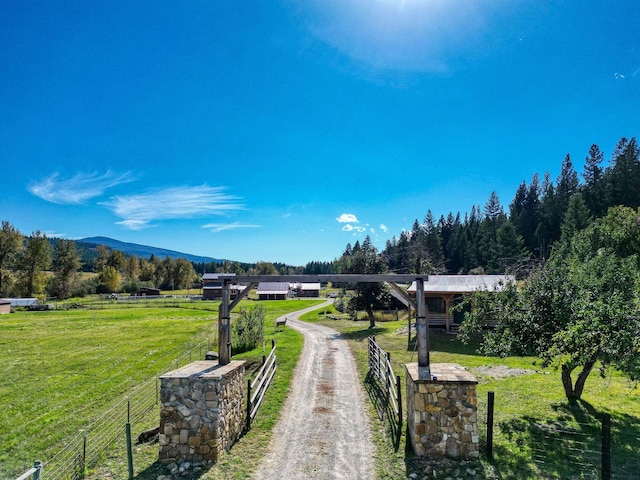 surrounding community featuring a rural view, a mountain view, fence, driveway, and a yard