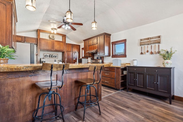 kitchen featuring ceiling fan, lofted ceiling, dark wood-type flooring, a breakfast bar, and freestanding refrigerator