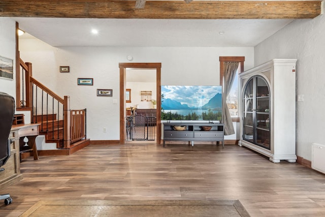 living area featuring beamed ceiling, stairway, baseboards, and wood finished floors