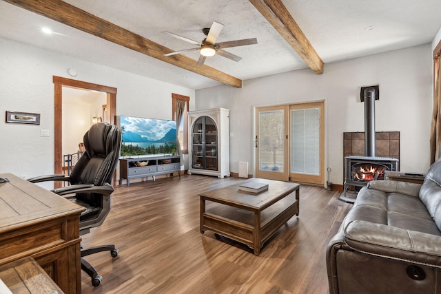 living room featuring a wood stove, ceiling fan, beam ceiling, and wood finished floors