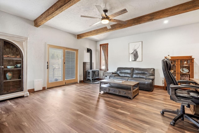 office area with a textured ceiling, wood finished floors, baseboards, beamed ceiling, and a wood stove