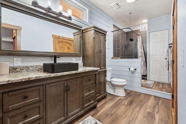 bathroom with toilet, wood finished floors, vanity, visible vents, and a tile shower