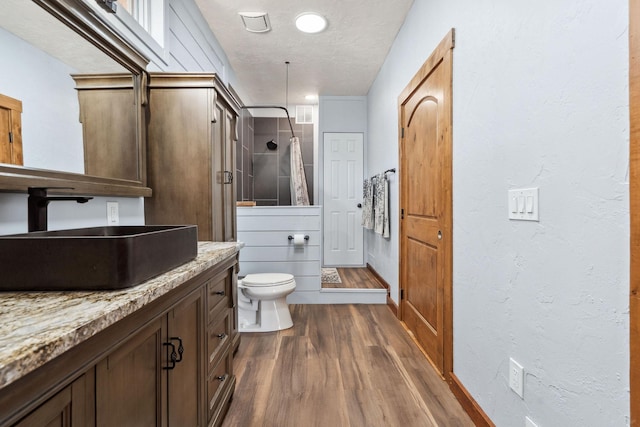 bathroom featuring a stall shower, toilet, wood finished floors, a textured ceiling, and vanity