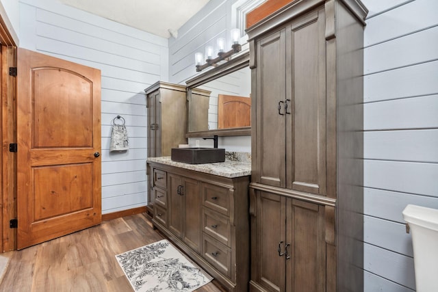 bathroom with toilet, wood walls, wood finished floors, and vanity