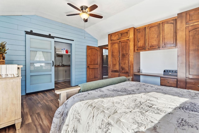 bedroom featuring vaulted ceiling, a barn door, dark wood-type flooring, and wooden walls