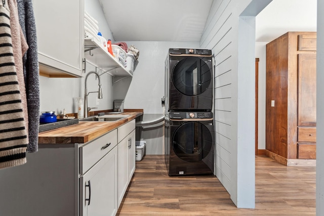 washroom featuring cabinet space, light wood-type flooring, a sink, and stacked washer and clothes dryer