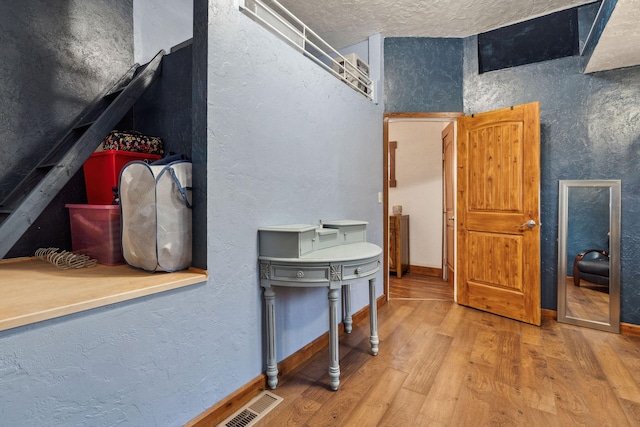 interior space featuring visible vents, a textured wall, a textured ceiling, wood finished floors, and baseboards