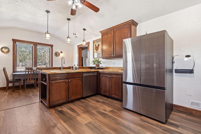 kitchen featuring dark wood-style floors, appliances with stainless steel finishes, a peninsula, vaulted ceiling, and a sink