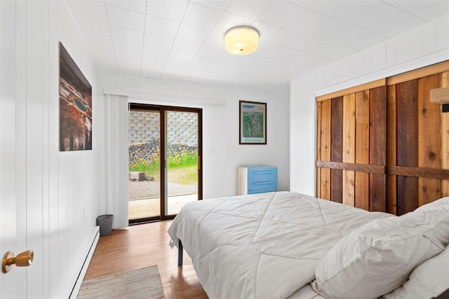 bedroom with a baseboard heating unit, access to outside, and wood finished floors