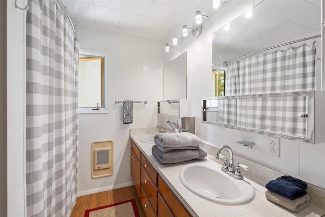 bathroom with double vanity, a sink, heating unit, and wood finished floors