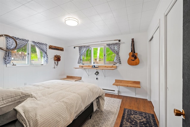 bedroom with a closet, multiple windows, baseboard heating, and wood finished floors