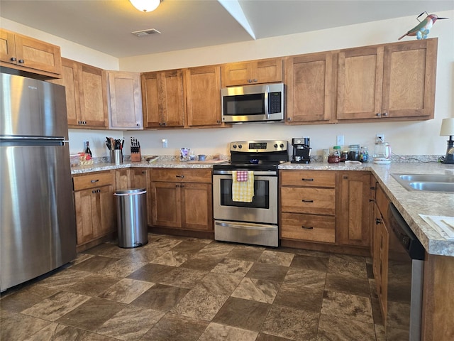 kitchen with appliances with stainless steel finishes, brown cabinetry, visible vents, and a sink