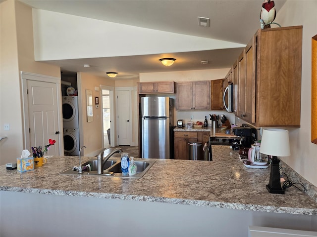 kitchen with stainless steel appliances, stacked washer and dryer, a sink, visible vents, and brown cabinets